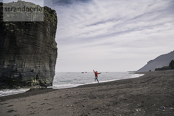 Frau am Lavastrand in Südost-Island  rennt und springt vor Freude