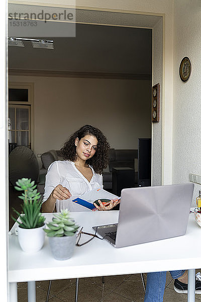 Junge Frau mit Notizblock und Laptop am heimischen Schreibtisch