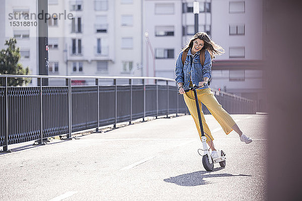 Glückliche junge Frau fährt Elektroroller auf einer Brücke