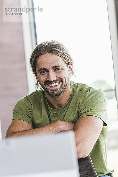 Porträt eines glücklichen jungen Geschäftsmannes  der im Büro sitzt