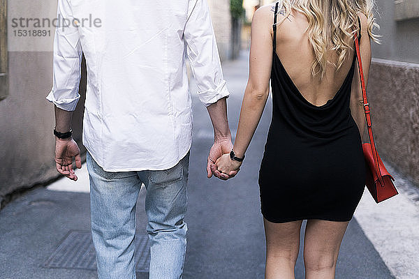 Rückansicht eines verliebten jungen Paares  das in der Stadt Händchen hält
