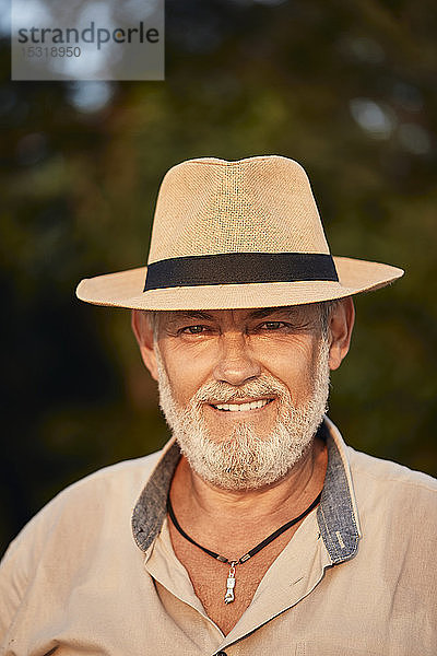 Porträt eines lächelnden älteren Mannes mit Sommerhut im Freien