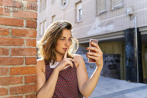 Junge Frau lehnt an Ziegelsteinmauer und nimmt ein Selfie