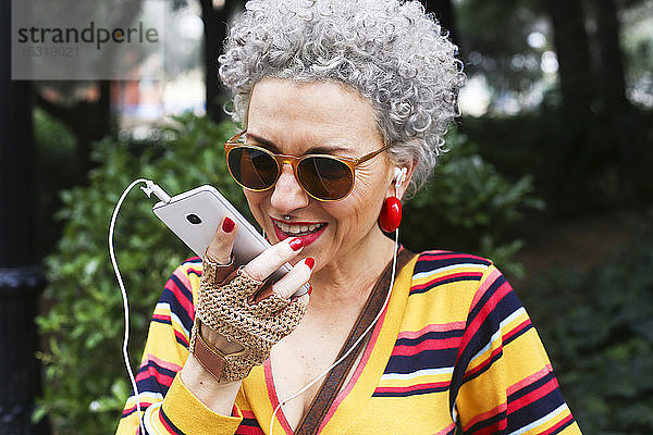 Porträt einer durchbohrten reifen Frau  die ein Smartphone im Freien benutzt