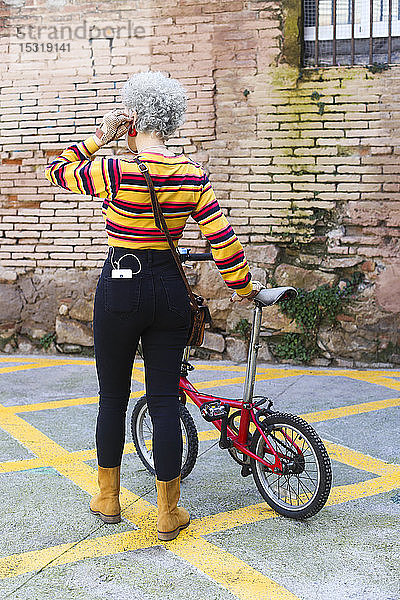 Rückenansicht einer Frau mit Fahrrad  die ein Smartphone in ihrer Tasche trägt