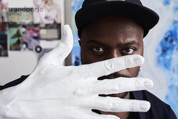 Schwarzer Künstler durch Finger einer weiß bemalten Hand in seinem Atelier