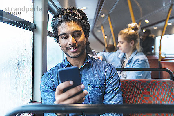 Porträt eines jungen Mannes  der mit dem Bus reist und auf sein Handy schaut  London  UK