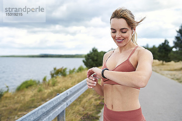 Porträt einer fitten Frau  die beim Joggen im Freien die Smartwatch kontrolliert