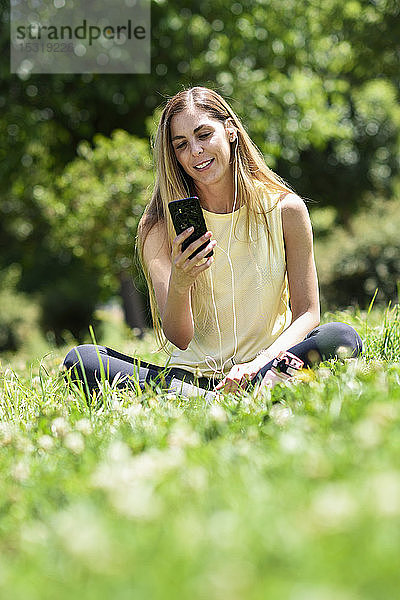 Frau  die ihr Smartphone benutzt und sich nach dem Sport im Gras eines Parks ausruht