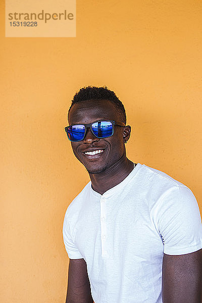 Porträt eines lächelnden jungen Mannes mit weißem T-Shirt und Sonnenbrille