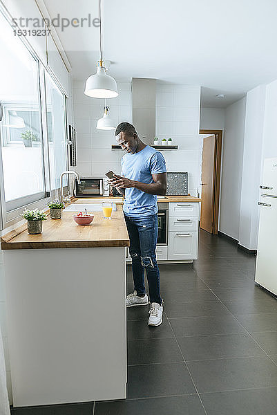Junger Mann benutzt Handy in der Küche zu Hause