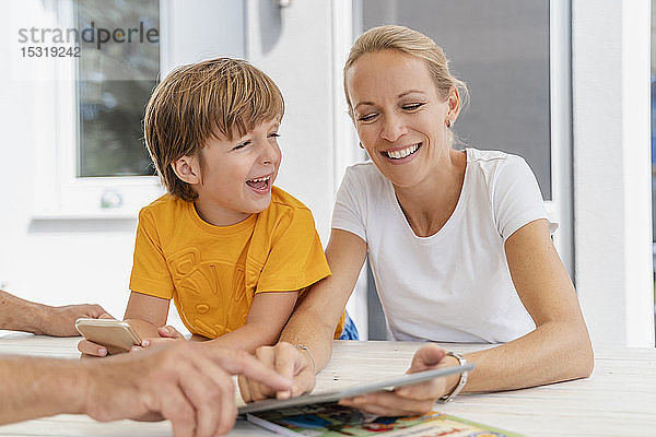 Glückliche Mutter und Sohn machen gemeinsam Hausaufgaben und benutzen Tabletten auf der Terrasse