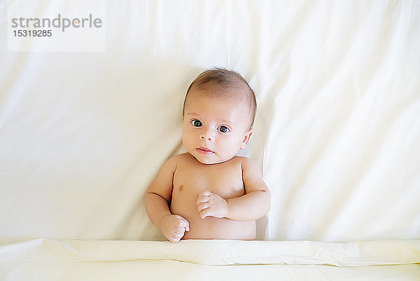 Porträt eines kleinen Jungen auf weißem Bettlaken liegend