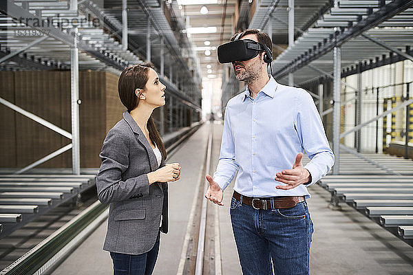 Geschäftsfrau im Gespräch mit einem Geschäftsmann mit VR-Brille in einer Fabrik