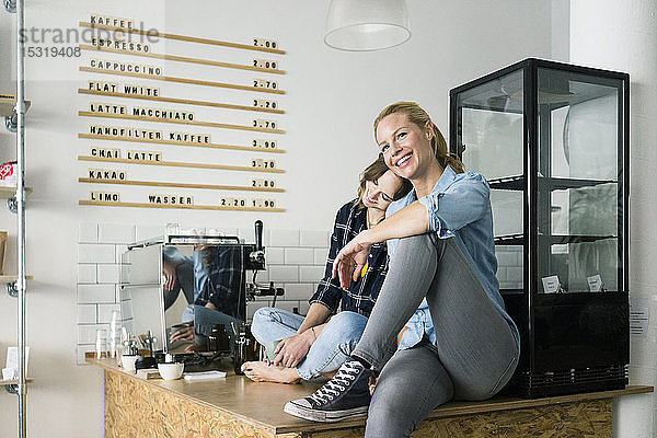 Zwei junge Frauen sitzen auf der Theke ihres Cafés