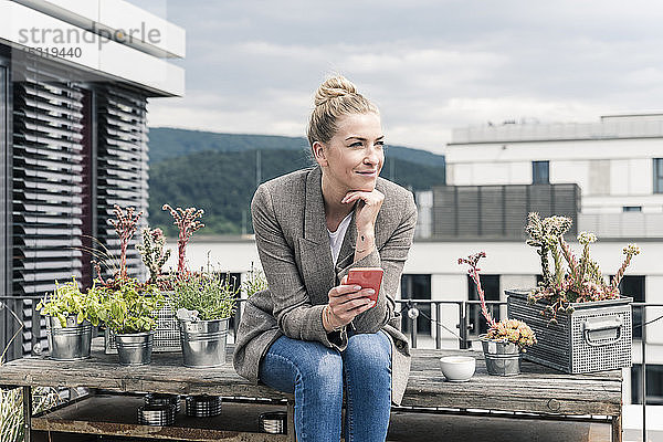 Geschäftsfrau mit Handy sitzt auf der Dachterrasse und macht eine Pause