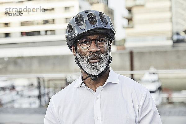 Porträt eines reifen Geschäftsmannes mit grauem Bart  der einen Fahrradhelm und eine Brille trägt