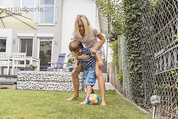 Glückliche Mutter und Sohn spielen im Garten Fussball