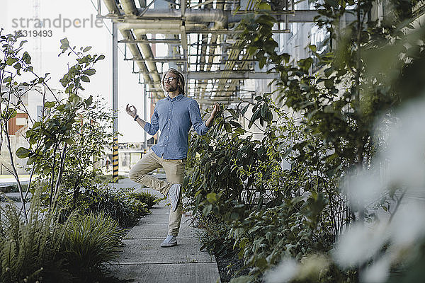 Junger Mann meditiert auf Bürgersteig inmitten von Pflanzen