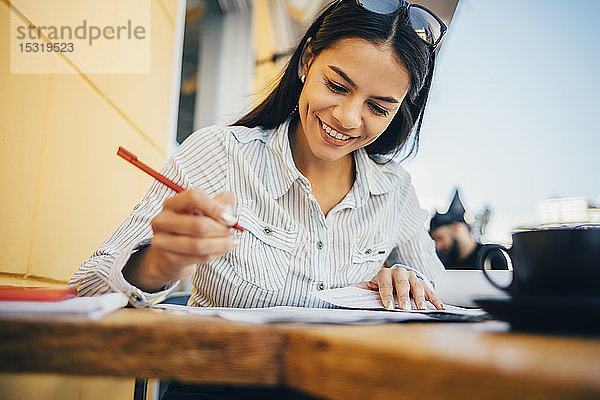 Lächelnde junge Frau macht Notizen in einem Cafe