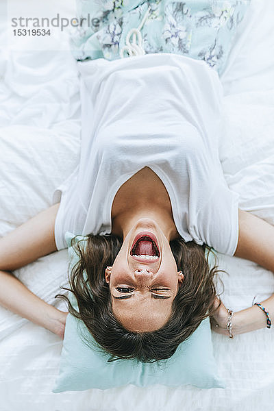 Draufsicht auf eine glückliche junge Frau  die zwinkernd im Bett liegt