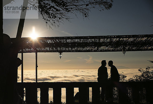 Silhouette eines schwulen Paares  das im Gegenlicht über den Wolken sitzt