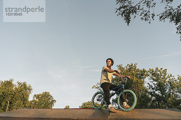 Junger Mann mit BMX-Rad im Skatepark bei einer Pause