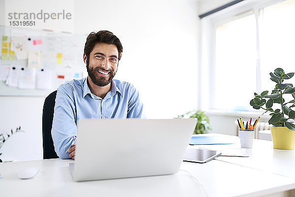 Porträt eines lächelnden Geschäftsmannes  der mit einem Laptop am Schreibtisch sitzt