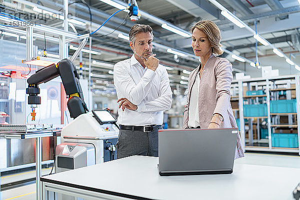 Geschäftsmann und Geschäftsfrau mit Laptop im Gespräch in einer modernen Fabrikhalle