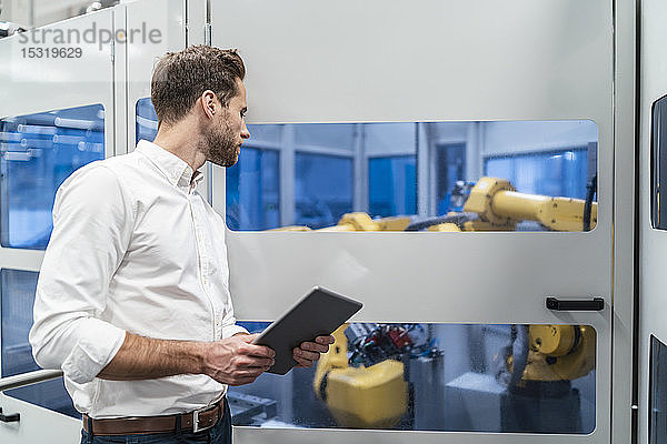 Geschäftsmann mit Tablette schaut sich Roboter in einer modernen Fabrik an