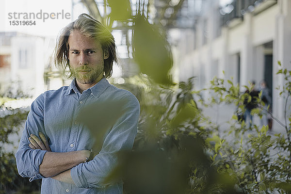 Porträt eines selbstbewussten jungen Mannes hinter einer Pflanze