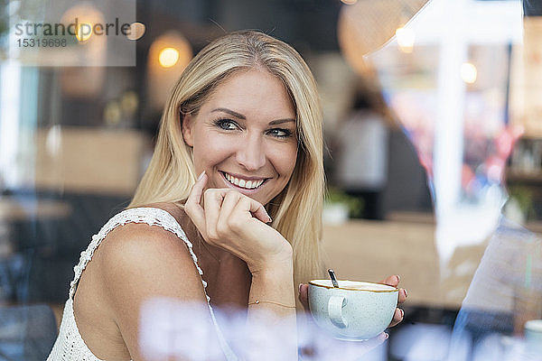 Porträt einer lächelnden blonden Frau  die in einem Café Kaffee trinkt