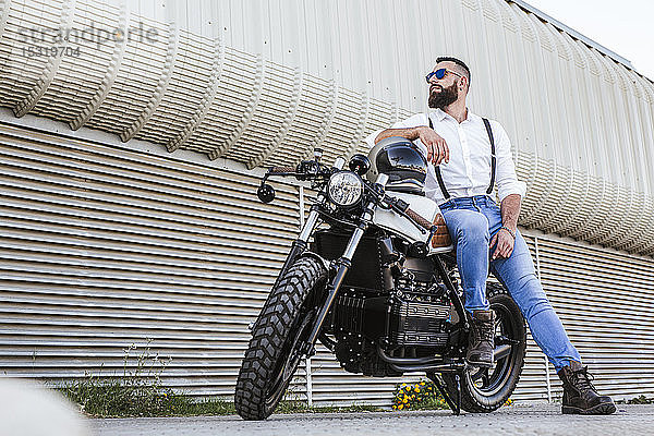 Bärtiger Motorradfahrer mit Sonnenbrille  der sich auf sein Motorrad stützt