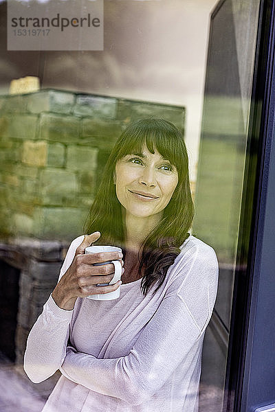 Porträt einer lächelnden Frau  die zu Hause eine Tasse Kaffee hält