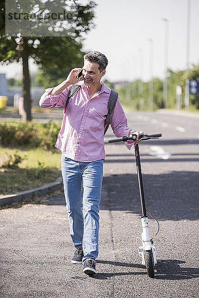 Geschäftsmann benutzt Smartphone  schiebt seinen E-Scooter