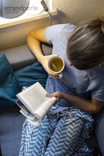 Draufsicht einer jungen Frau  die zu Hause auf der Couch ein Buch liest