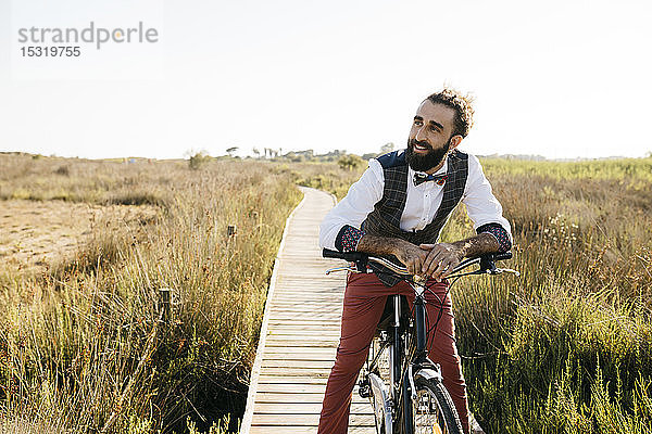 Gut gekleideter Mann mit seinem Fahrrad auf einem Holzsteg auf dem Land  der eine Pause macht
