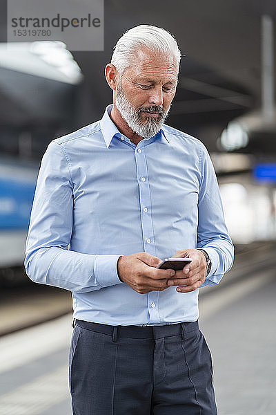Älterer Geschäftsmann benutzt Mobiltelefon am Bahnsteig