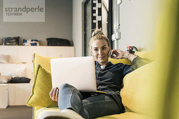 Lässige Geschäftsfrau mit Laptop auf der Couch in der Büro-Lounge