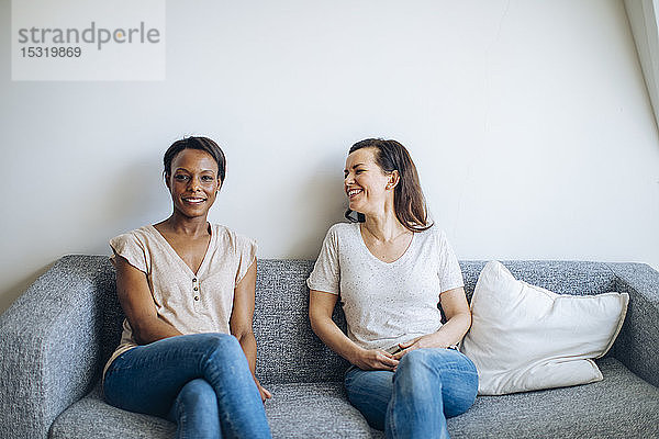 Zwei lächelnde Frauen sitzen zu Hause auf der Couch