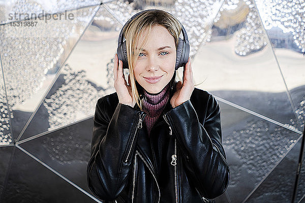 Porträt einer lächelnden jungen Frau  die mit drahtlosen Kopfhörern Musik hört