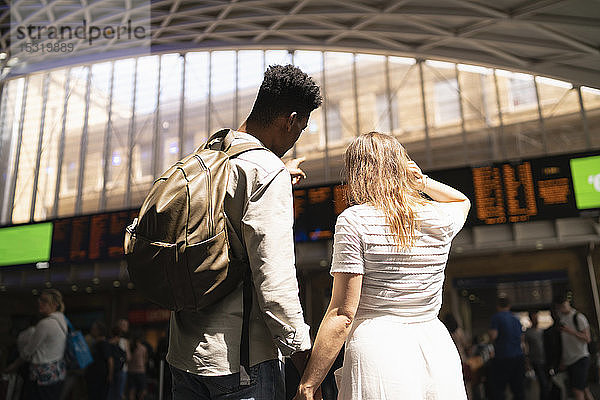 Rückansicht eines jungen Paares mit Blick auf die Anzeigetafel des Bahnhofs  London  UK