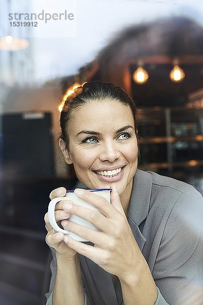 Porträt einer Geschäftsfrau hinter einer Fensterscheibe in einem Café beim Kaffeetrinken