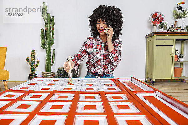 Frau malt Möbel mit Pinsel und benutzt Smartphone zu Hause