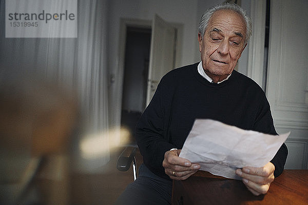 Älterer Mann sitzt zu Hause am Tisch und liest eine Zeitung