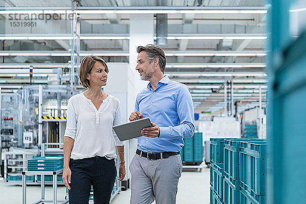 Geschäftsmann und Geschäftsfrau mit Tablettengespräch in einer Fabrikhalle