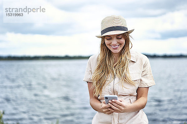 Glückliche Frau beim Handy-Checken am Seeufer