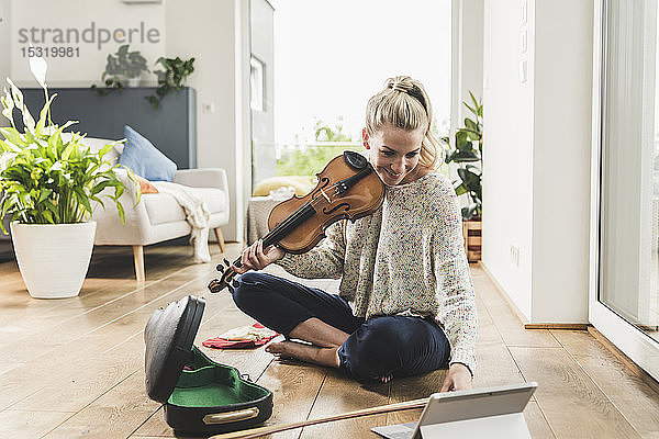 Frau mit Tablette sitzt zu Hause auf dem Boden und spielt Geige