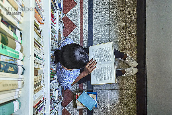 Draufsicht auf eine junge Frau  die auf dem Boden sitzt und in der Nationalbibliothek in Maputo  Mosambik  ein Buch liest