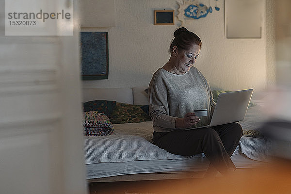 Ältere Frau sitzt zu Hause im Bett und benutzt Kreditkarte und Laptop